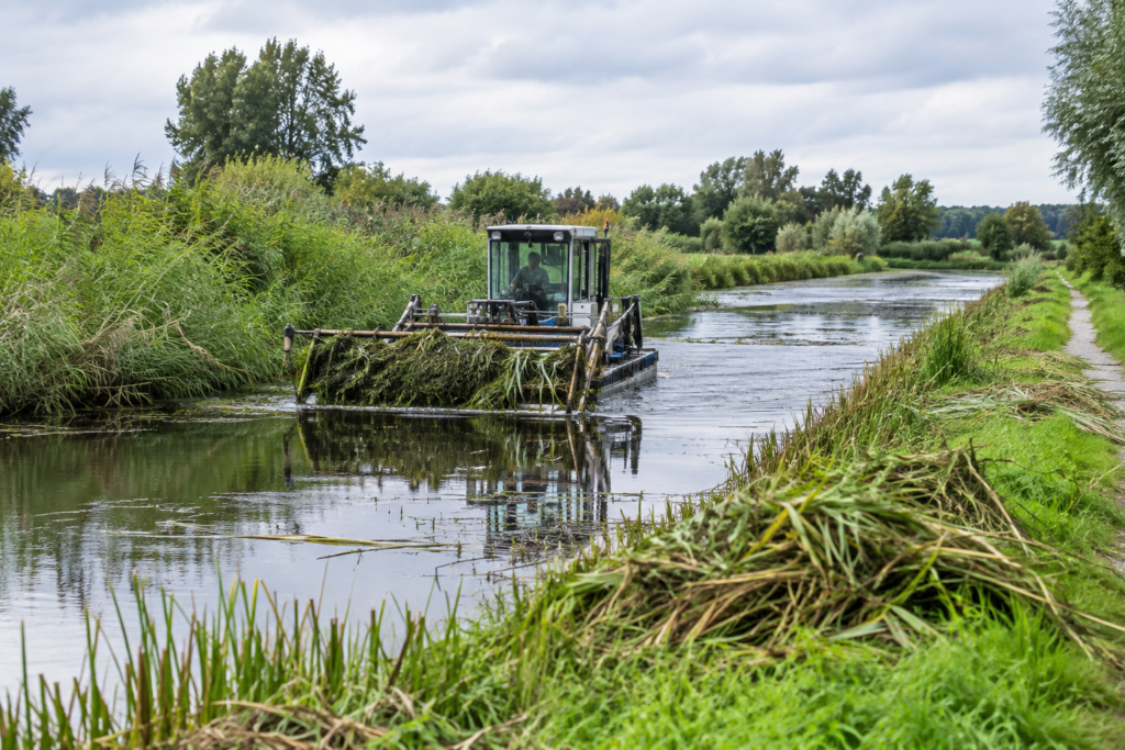 Maaimachine verwijdert waterplanten uit een brede sloot